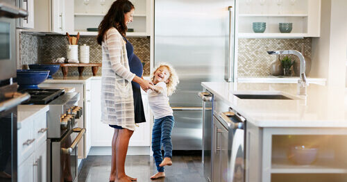 Mother and child in kitchen, surrounded by home appliances.