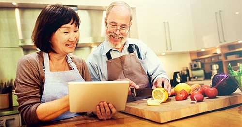 Older couple consults their tablet device to follow along with a cooking course.