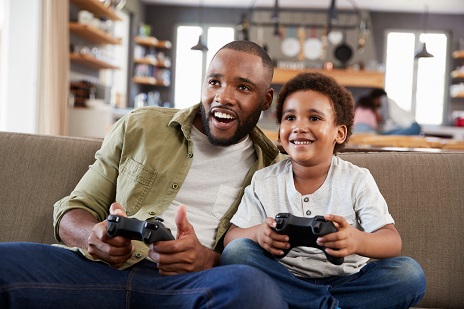 Man and son sitting on couch smiling playing video games.