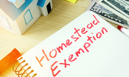 Notepad with "Homestead Exemption" written on it - model house and dollar bills also on desk.