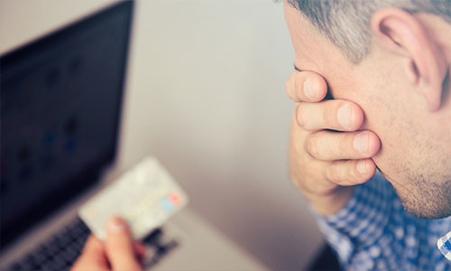 Upset man with face in one hand, credit card in another, worried he may be the victim of identity theft.