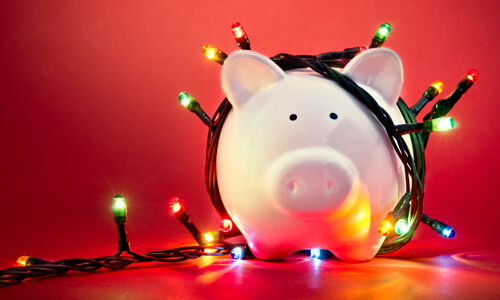 Piggy bank with Christmas Lights draped around it, red background.