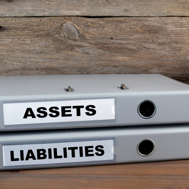 Two binders, one labeled "Assets" and the other labeled "Liabilities" lying on a desk.