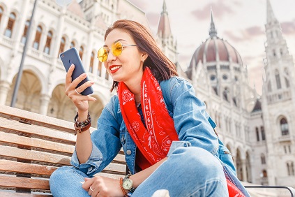 A Young Woman wearing a red scarf and sunglasses while traveling in Europe looks at her cell phone