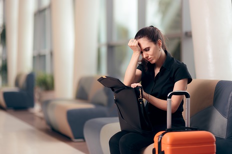 Woman sitting in airport lobby with lobby, looking in her bag, realizing she forgot something.