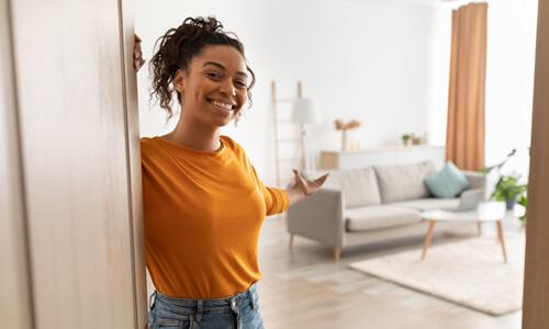 Smiling woman standing at door of new apartment, welcoming you inside.