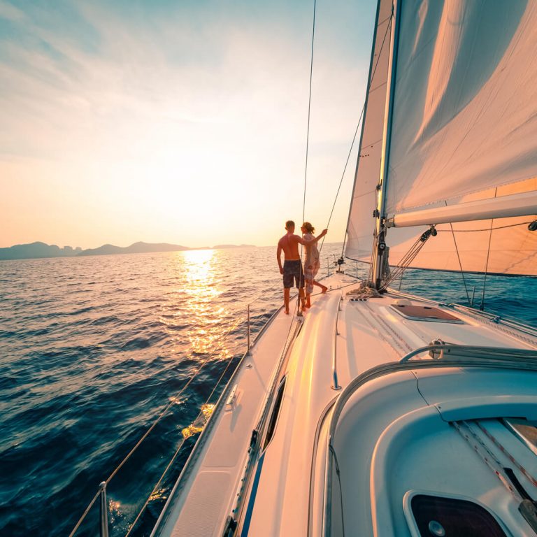 Couple on sailing yacht looks into sunset.