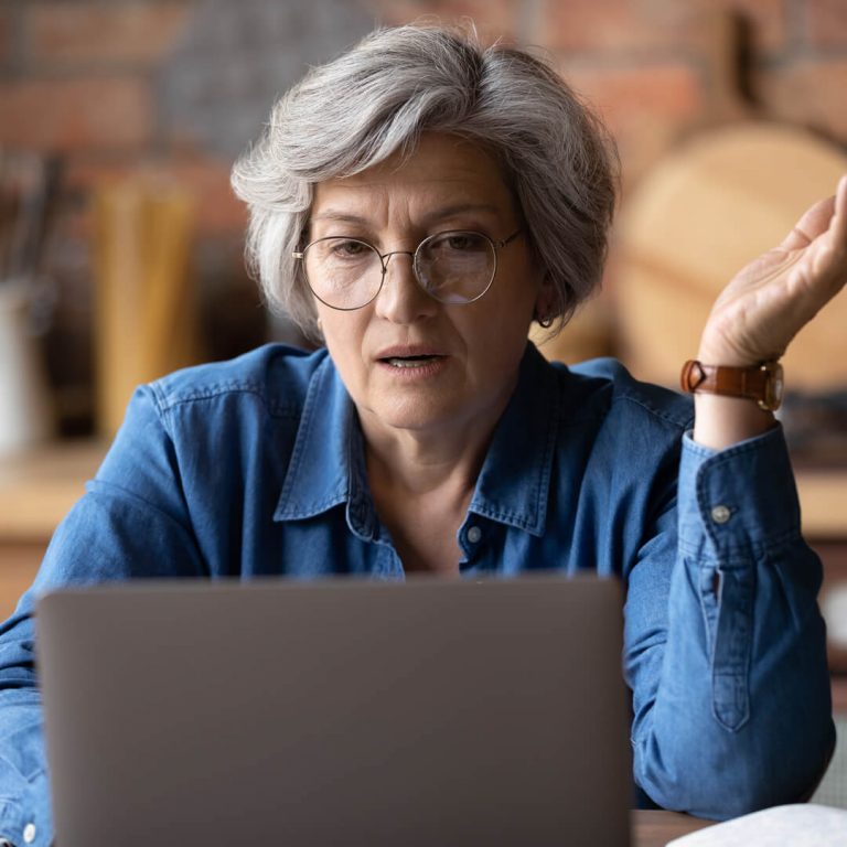 Older woman at her laptop looking concerned after possibly falling victim to a survey scam.