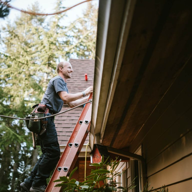 Man on ladder making repairs to his home roof.