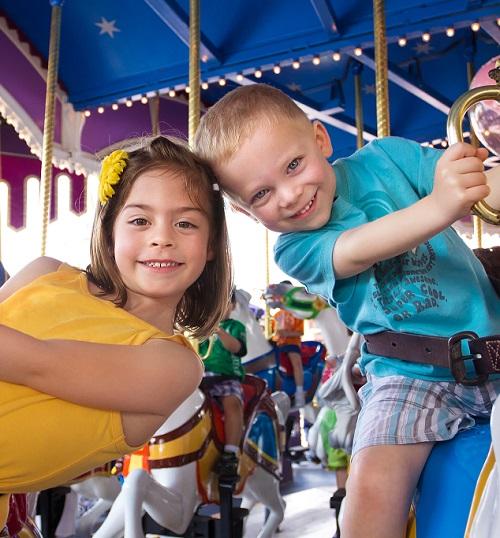 Two excited children ride the carousel at a theme park.
