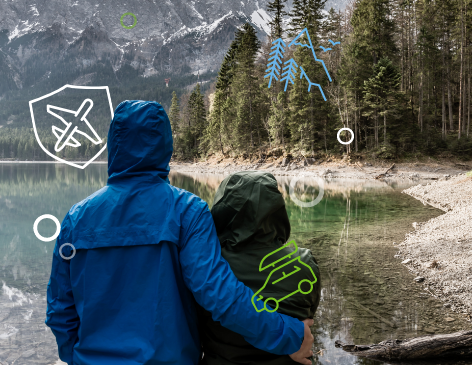Two travelers in raincoats admire a lake and mountain view secure in their travels by having Quorum's travel insurance.