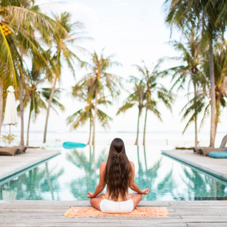 Woman on wellness retreat, doing yoga at resort pool.