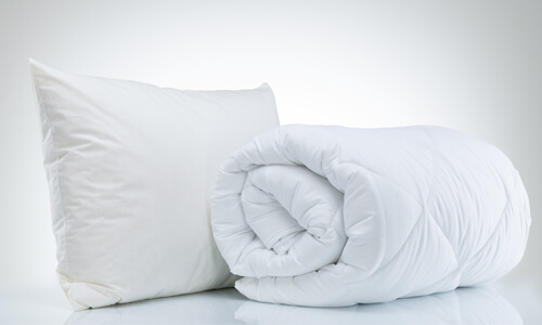White pillow and rolled up duvet on white background - items that are heavily discounted in January during the White Sale.