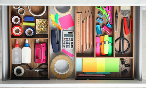 Office and school supplies organized in a desk drawer.