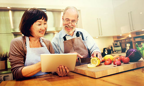 Older couple consults their tablet device to follow along with a cooking course.