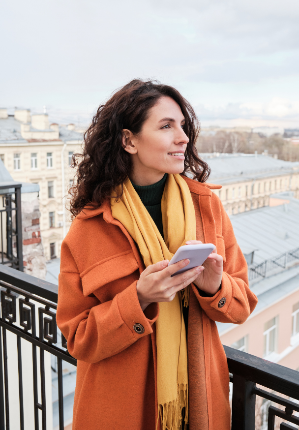 Smiling woman holding a smartphone overlooks a European city.